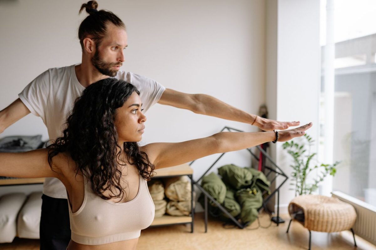 Arassoc A yoga instructor helps a woman with her Warrior Pose in a serene indoor studio.