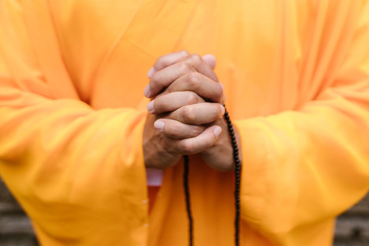service-01 Close-up of hands in prayer wearing yellow robes, sign of Zen meditation and peace.